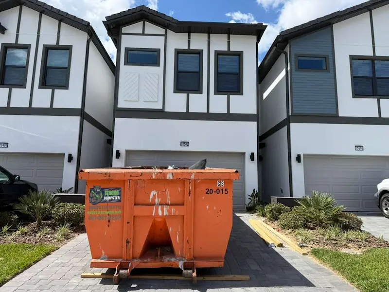 Orange Dumpster Strong roll-off dumpster on a paver driveway in front of Central Florida townhomes