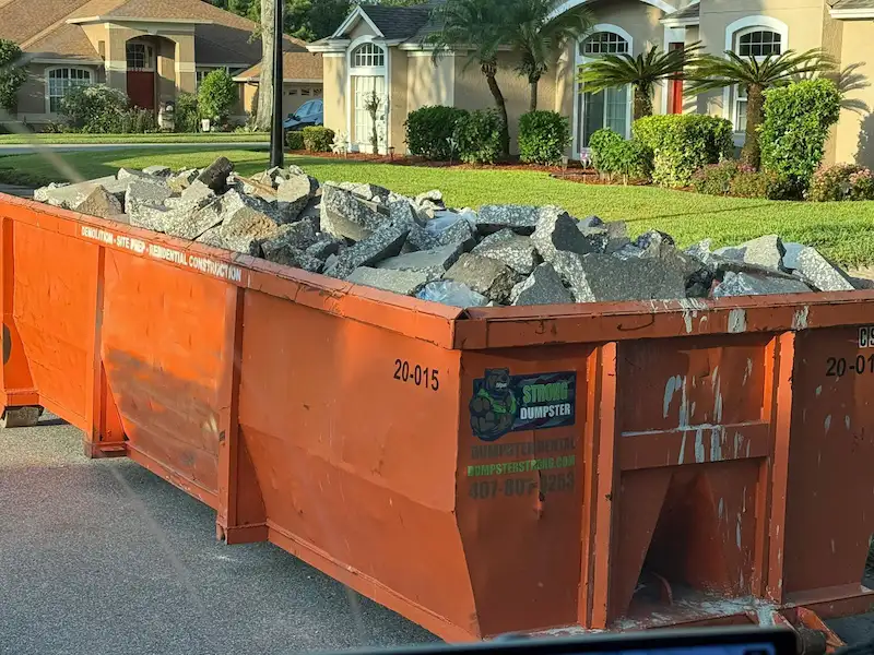 Dumpster Strong 20-yard concrete dumpster on an Orlando residential driveway during a concrete driveway removal job, filled with broken slab and rebar