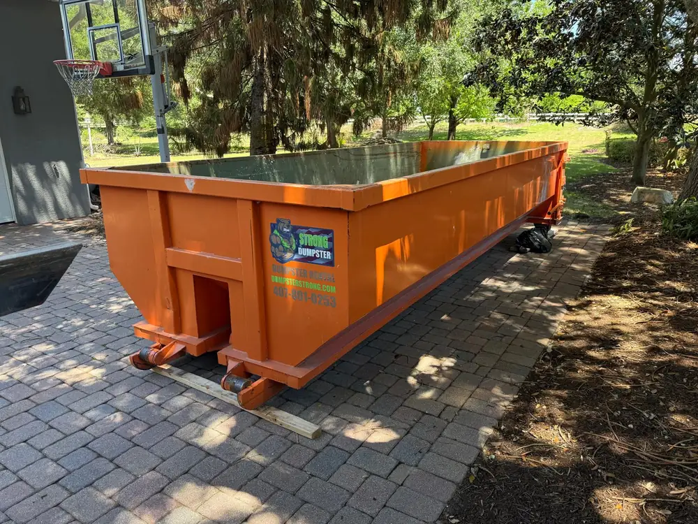 Dumpster Strong roll-off dumpster on a Clermont FL estate paver driveway beside a basketball court, large-property renovation