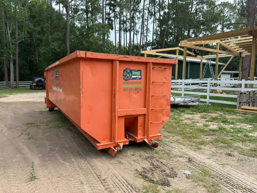 Dumpster Strong roll-off dumpster on a large wooded Longwood FL property during a barn and outbuilding construction project