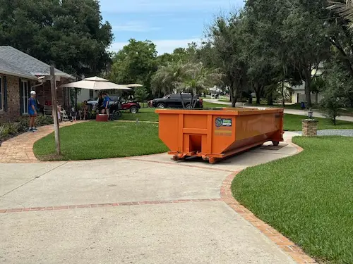 Orange Dumpster Strong 20-yard roll-off dumpster on a Windermere FL residential driveway with paver-edged concrete and lush landscaping