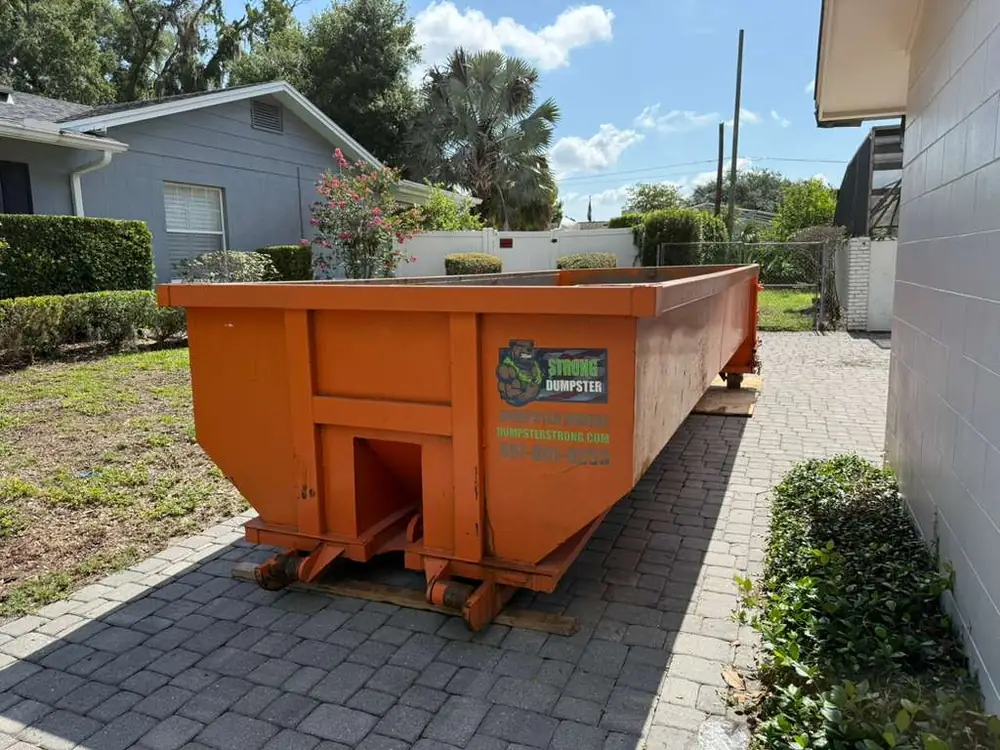Dumpster Strong roll-off dumpster on a Winter Garden FL brick-paver driveway with plywood board protection, residential remodel