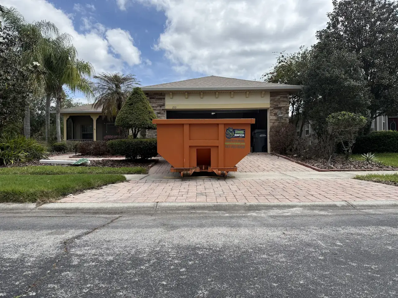 Orange Dumpster Strong roll-off dumpster on a residential driveway in Orlando, FL