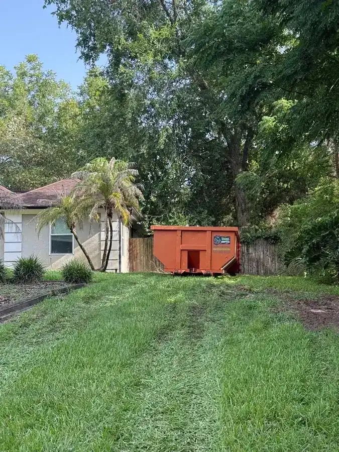 Yard-waste dumpster on a backyard lawn for a Kissimmee-area landscaping and storm-prep cleanup